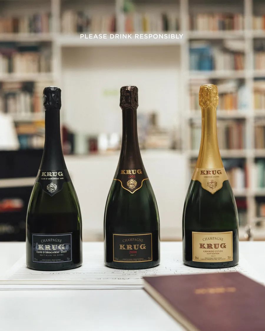 Tres botellas de champán Krug delante de una estantería de libros