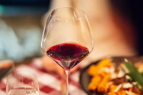 Copa de vino tinto de RIEDEL en una mesa puesta, junto a un plato de pasta